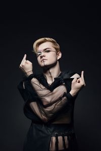 Portrait of man showing obscene gesture against black background