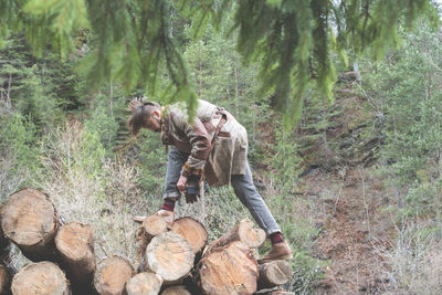 Side view of young man standing on logs in forest