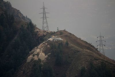 Low angle view of electricity pylon on mountain against sky