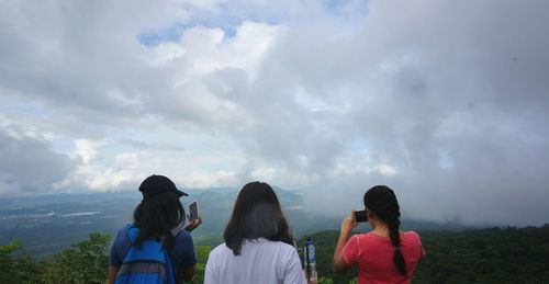 Rear view of women standing on landscape against cloudy sky