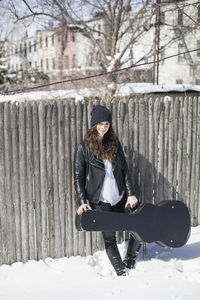 Young woman carrying a guitar case through the snow