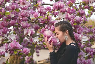 Young woman smelling pink flowers blooming during springtime
