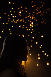 Low angle view of woman against illuminated lighting equipment at night