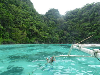 People swimming in sea against trees