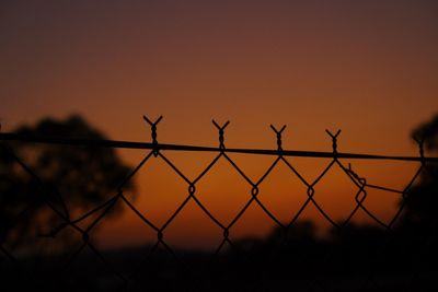 Silhouette fence against sky during sunset