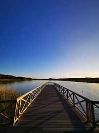 Footbridge over lake against clear blue sky