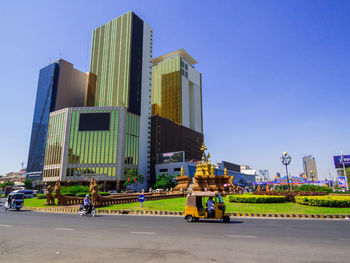 People on road by buildings against clear sky in city