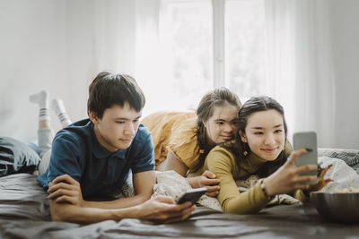 Down syndrome woman lying down with siblings using smart phone on bed at home