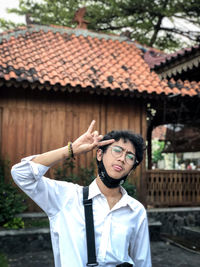 Portrait of young man gesturing while standing against house