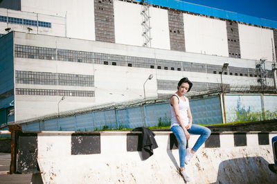 Young woman sitting on barricade against factory