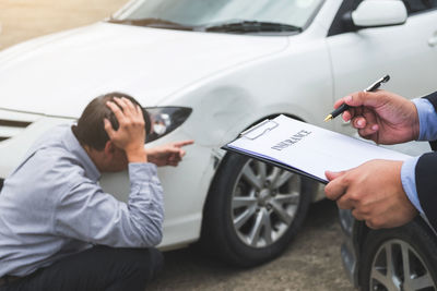 Cropped image of insurance agent with document by owner showing damaged car