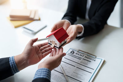 Midsection of real estate agent giving key to client in office