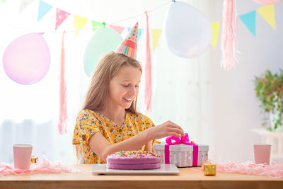 Girl unboxing gift sitting by cake at home