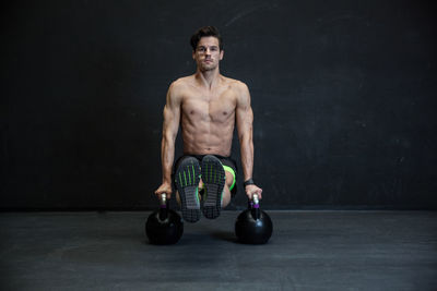 Portrait of shirtless man exercising with kettlebells in gym