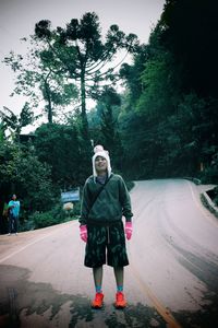 Portrait of young man standing on road against trees