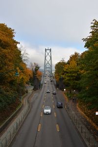 Cars on road by bridge against sky