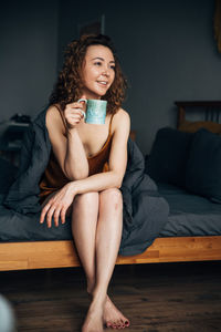 Young brunette enjoys her morning coffee while sitting in bed in a cozy room