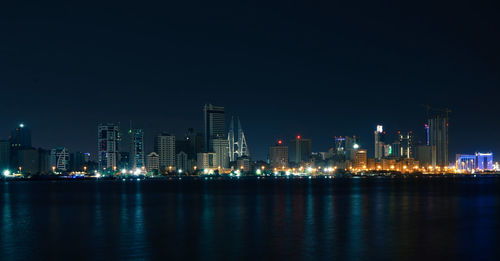 Illuminated city by sea against sky at night