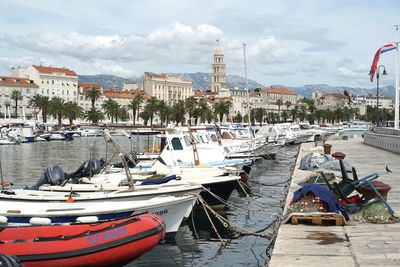 Boats moored at harbor against sky in city