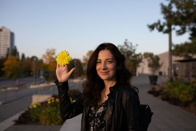 Portrait of smiling woman holding yellow flower against clear sky