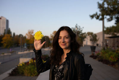 Portrait of young woman holding plant against sky