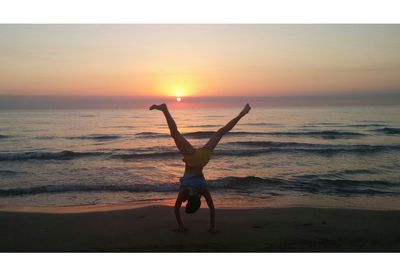 Full length of playful boy practicing handstand at beach during sunset