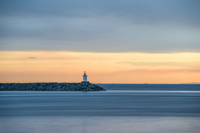 Lighthouse by sea against sky during sunset