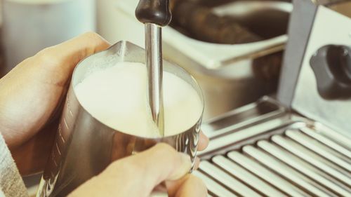 Cropped hands holding milk in jug at cafe