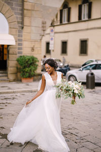 Full length of bride holding flower bouquet on street