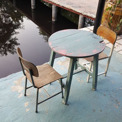 High angle view of empty chairs and table by lake