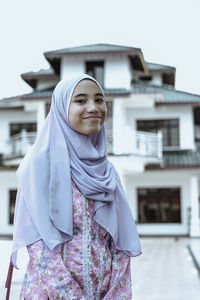 Portrait of smiling young woman standing against house