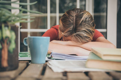 Tired boy with head own next to books and coffee cup at desk