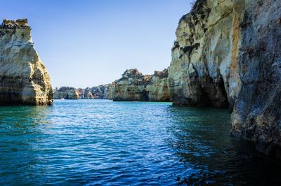 Rock formations by sea against clear blue sky