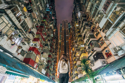 Rear view of woman standing amidst illuminated buildings in city