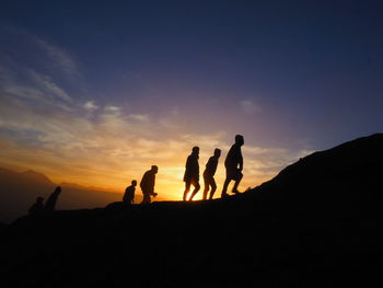 Silhouette people on land against sky during sunset