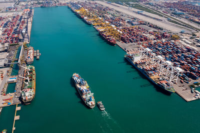 Aerial top view container ship and tugboat sailing in sea and commercial port working crane bridge 
