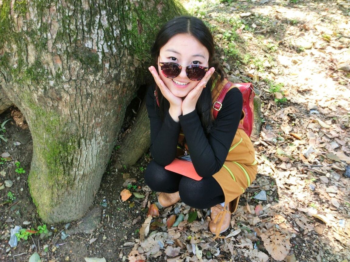 portrait, looking at camera, lifestyles, young adult, person, front view, casual clothing, standing, leisure activity, smiling, young women, sunglasses, outdoors, day, high angle view, tree, happiness, nature