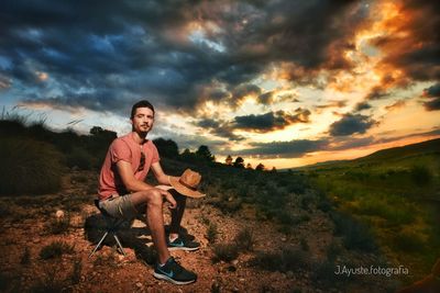 Man sitting on field against sky during sunset