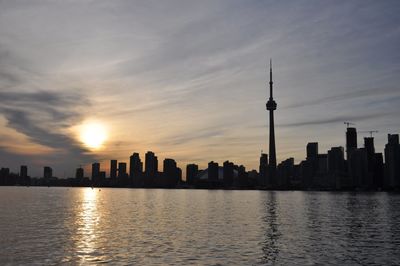 Silhouette cn tower amidst buildings in front of sea against sky during sunset