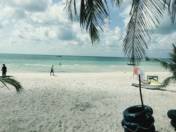 Tourists on beach against cloudy sky