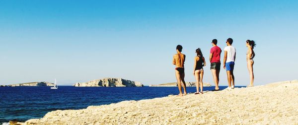 Rear view of people at beach against clear blue sky