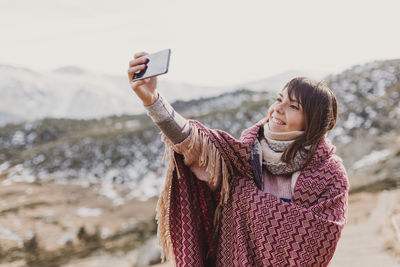 Side view of woman taking selfie while standing on mountain