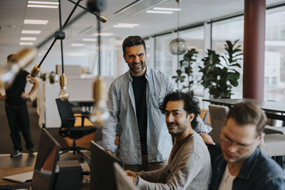 Portrait of smiling male colleagues by businessman working at desk in office