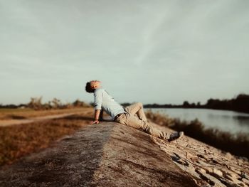 Man sitting on rock by lake against sky