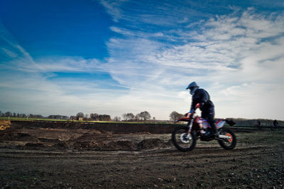 Person riding motocross on field against sky