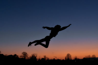 Silhouette man jumping against sky at sunset