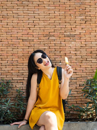 Full length of young woman sitting against brick wall