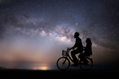 Silhouette people with bicycle against sky at night