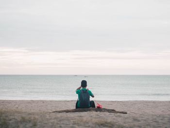 Rear view of woman sitting on beach against sky