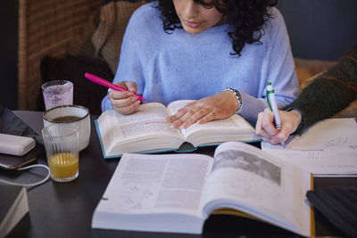 Midsection of woman writing in book at table